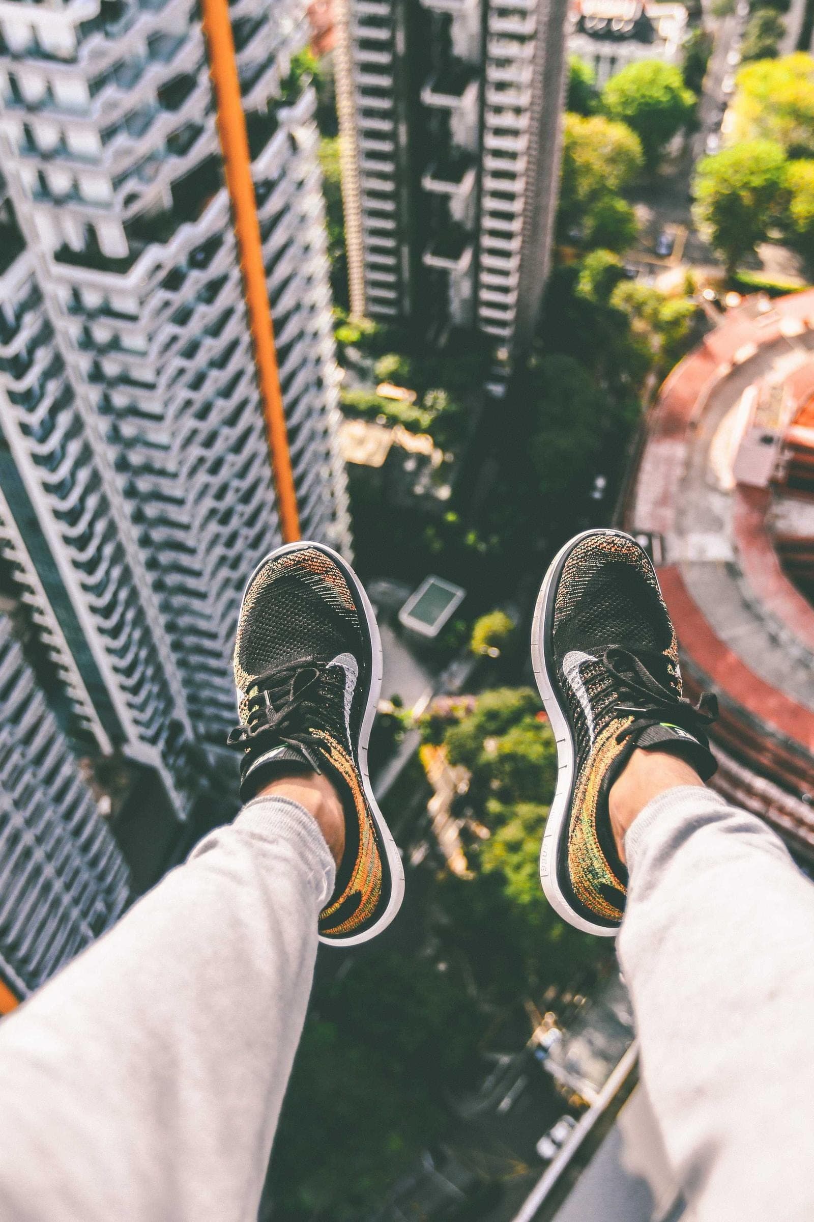 looking straight down past a pair of sneakers from a high ledge, apartment towers and treetops a long way below
