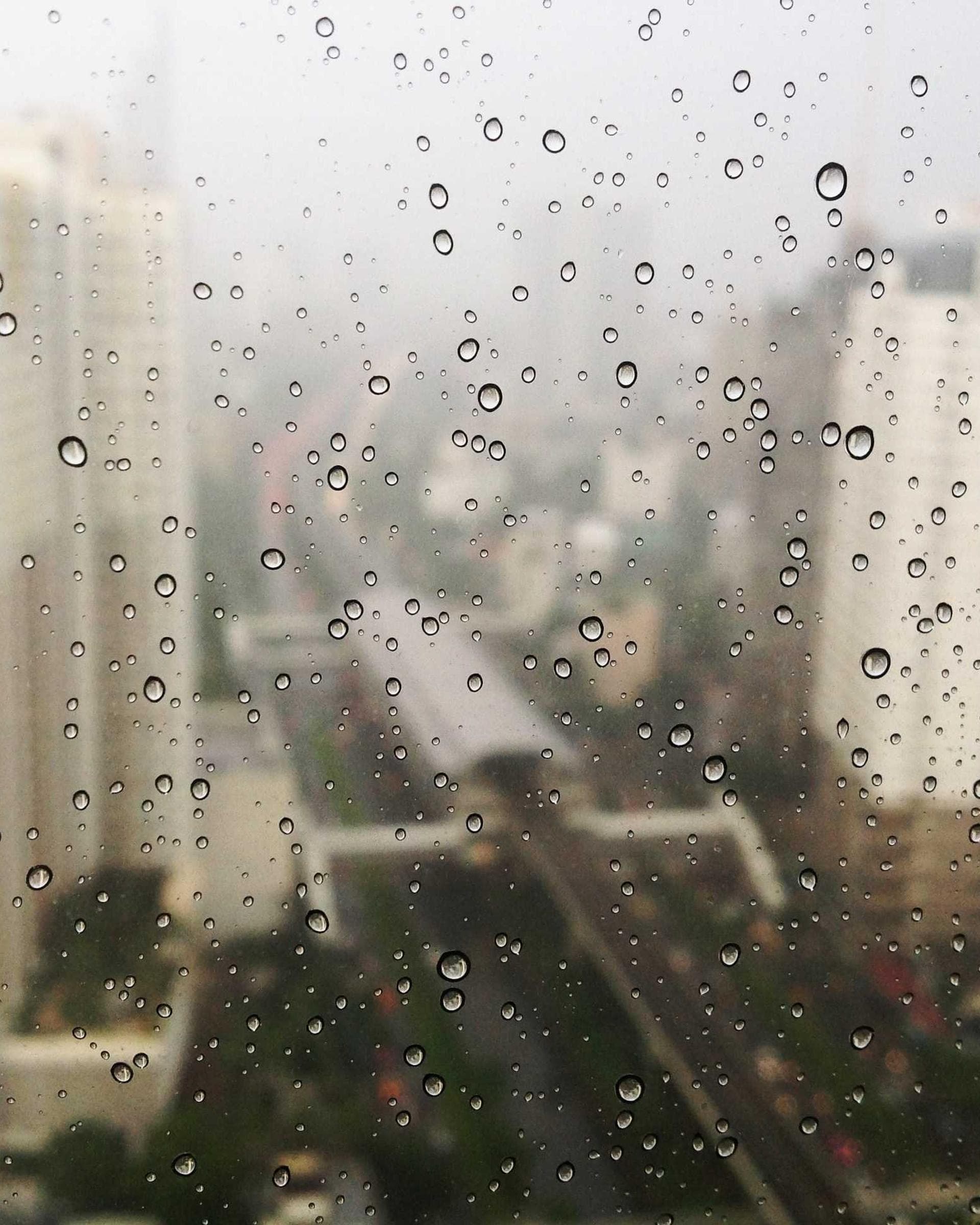 a city through a window beaded with rain, the drops sharp and the towers behind them soft